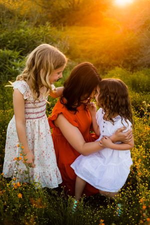 A mom and her two children dressed for spring nestled down in a field of desert flowers during a golden sunset for their family portraits.