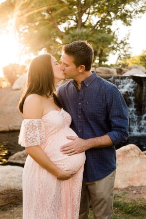 A pregnant couple kissing in front of a beautiful waterfall at sunset for their maternity photoshoot.