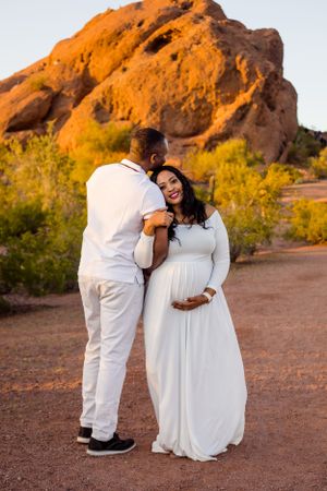 Maternity woman and her husband at Papago standing in front of the Papago park mountain during sunset for their maternity outdoor session.