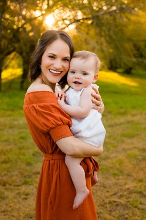 Mom holds and snuggles her baby during the golden glow of sunset in a pretty green field for family portraits.