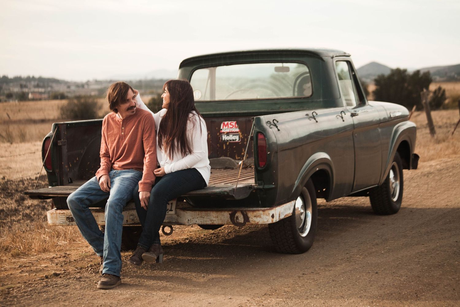 Couple sitting on the tailgate of a vintage pickup truck in a rural setting.