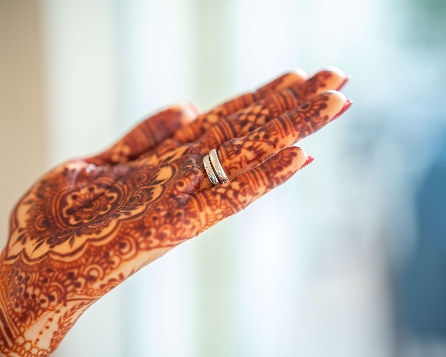 Wedding ring placed on hand decorated with intricate henna mehndi design.