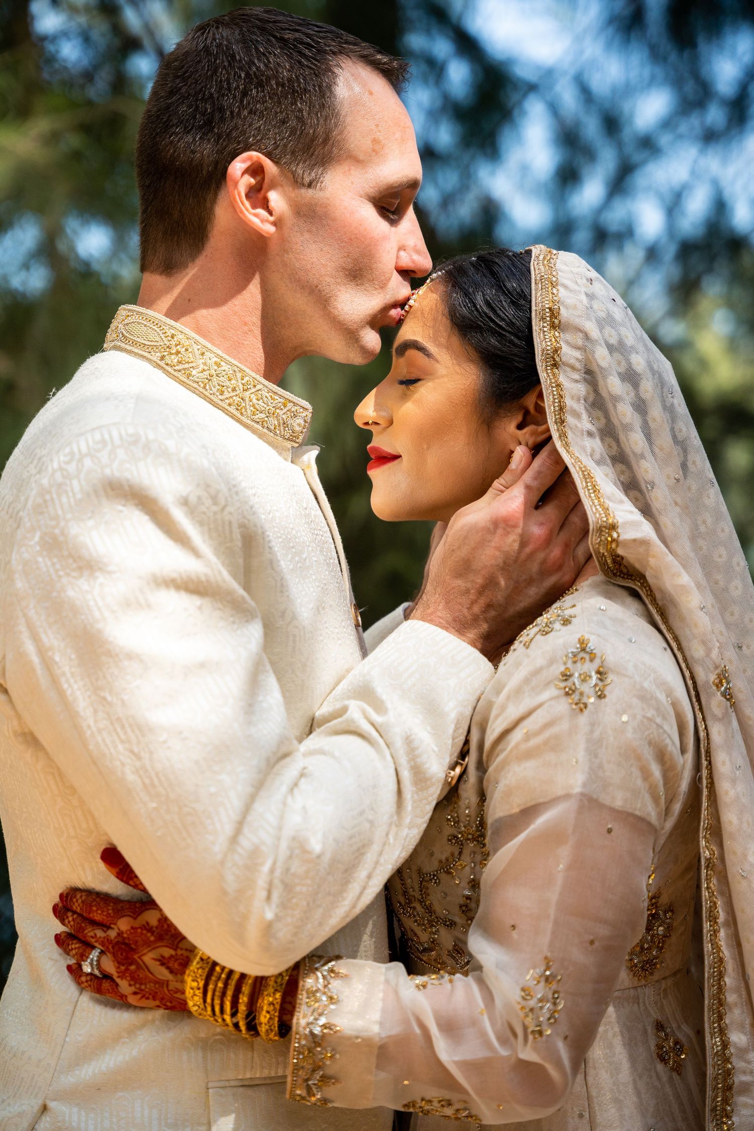 Wedding couple in traditional white and gold attire sharing tender moment.