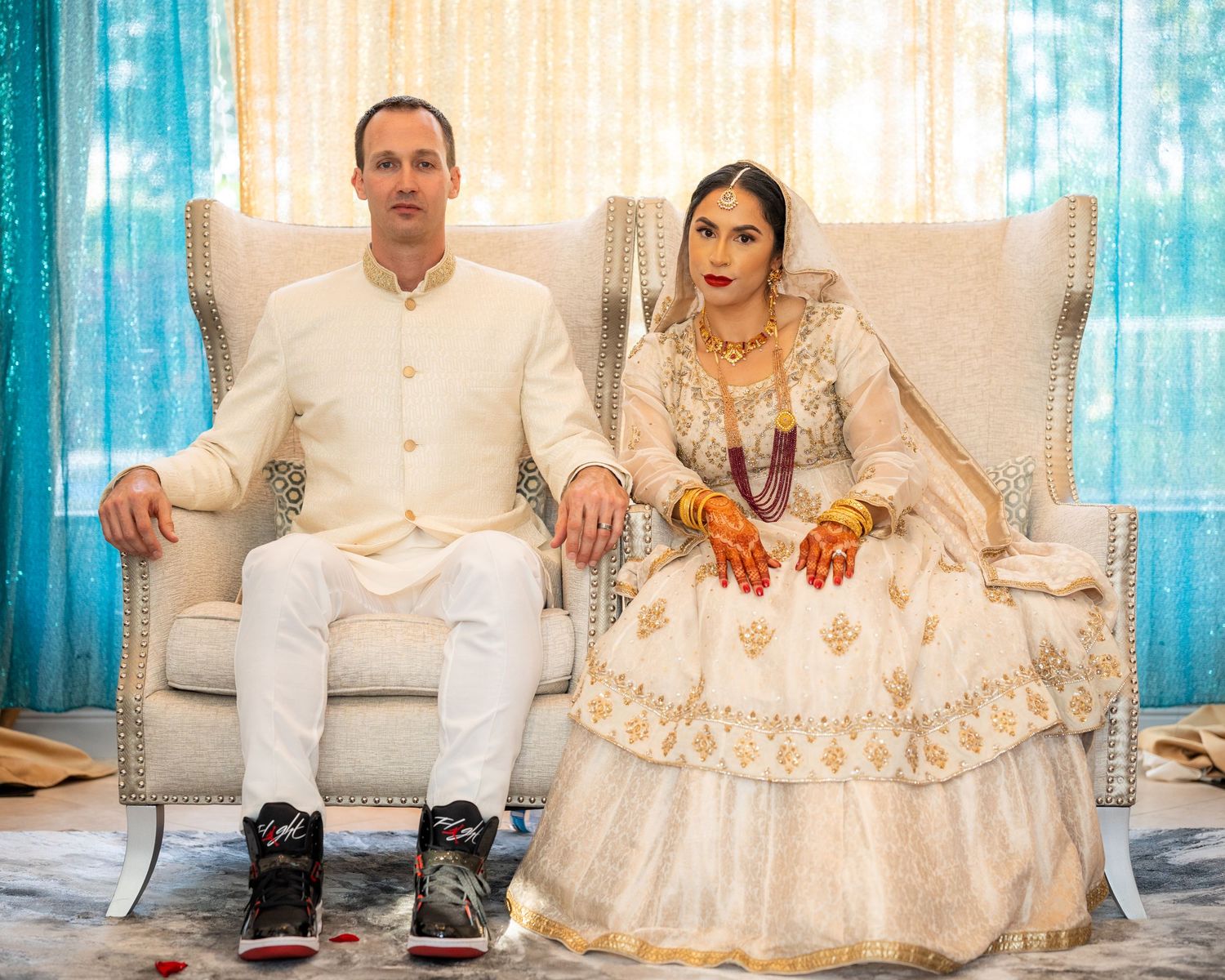 Couple seated at traditional South Asian wedding ceremony in white and cream formal attire.