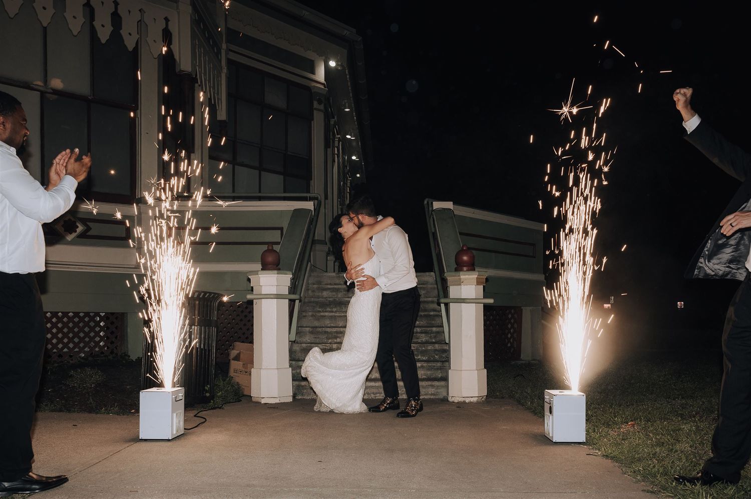 Newlyweds share a moment while cold sparklers create a magical backdrop at their nighttime celebration.