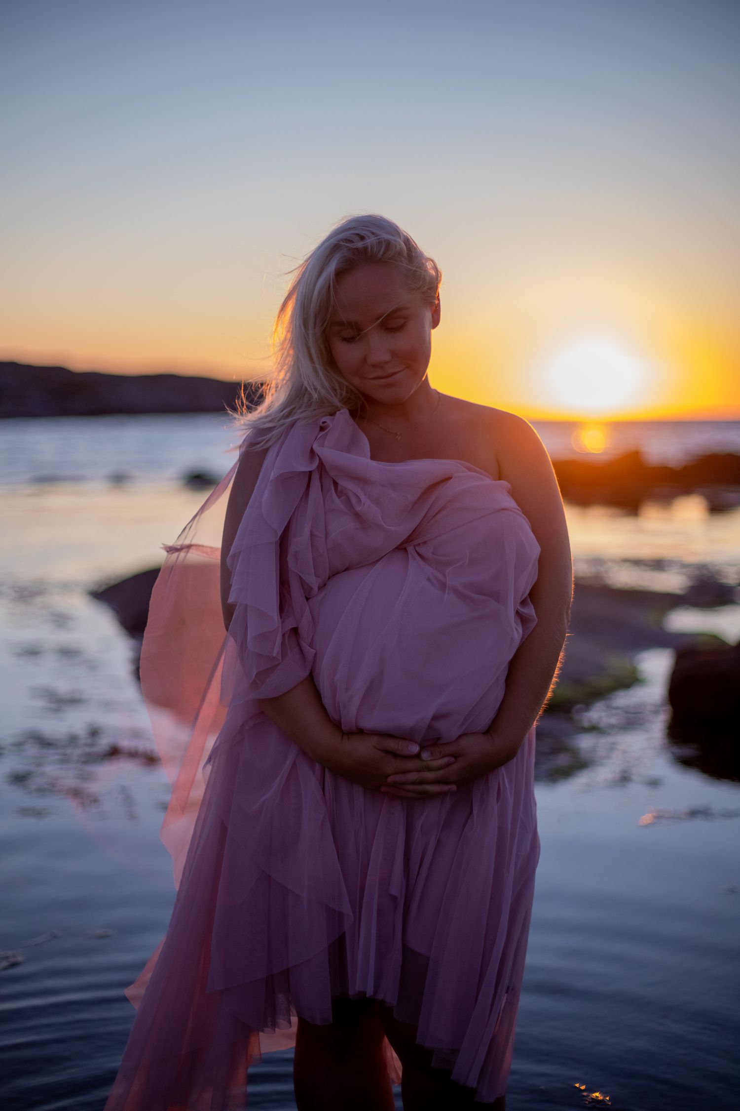 Romantic beach maternity session with soft pink dress during sunset.
