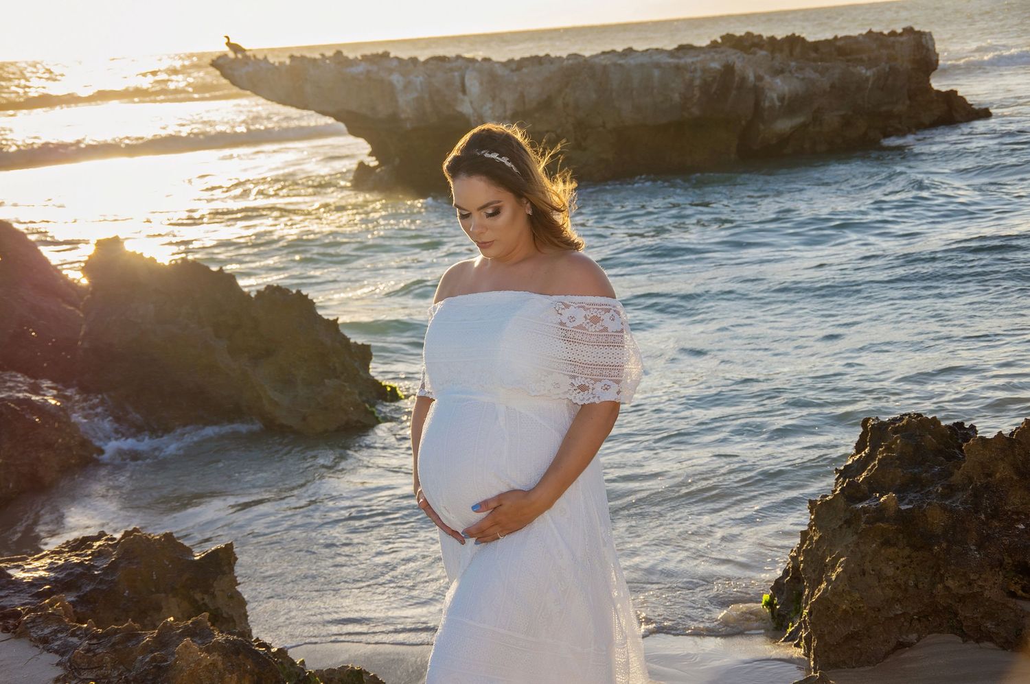 woman embracing pregnant belly on beach
