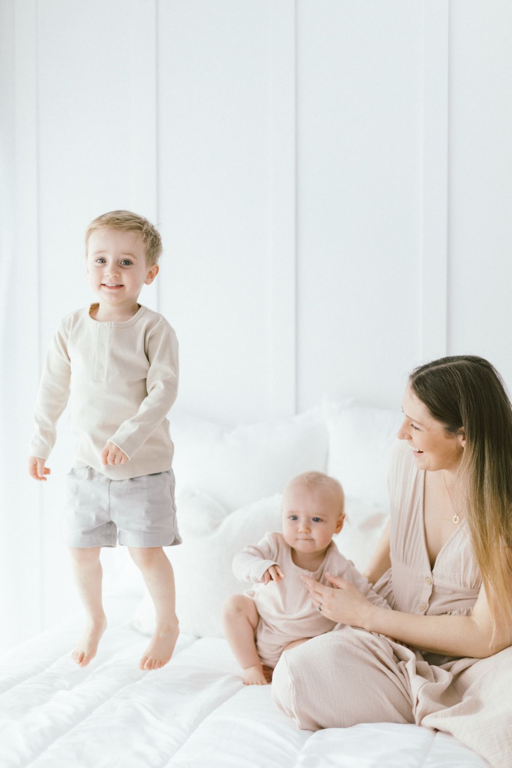 Intimate family portrait on white bed with soft natural lighting.