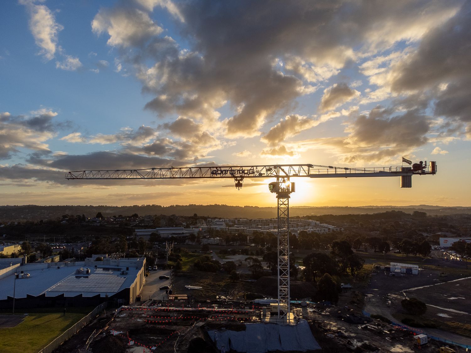 Construction crane silhouetted against a stunning golden sunset sky over an urban Australian cityscape.
