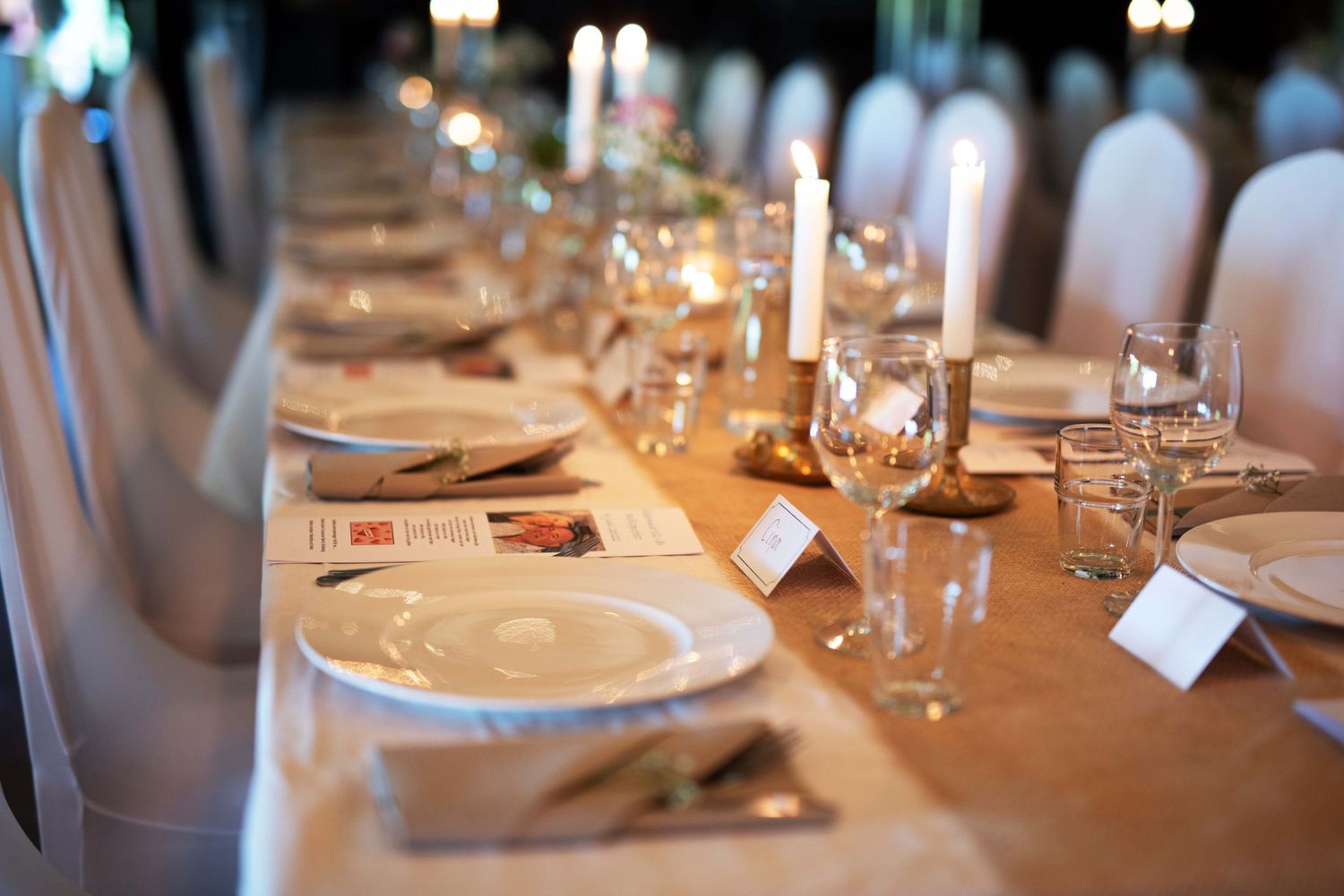 Elegantly set long banquet table with candles, white plates, and glassware for a wedding reception.