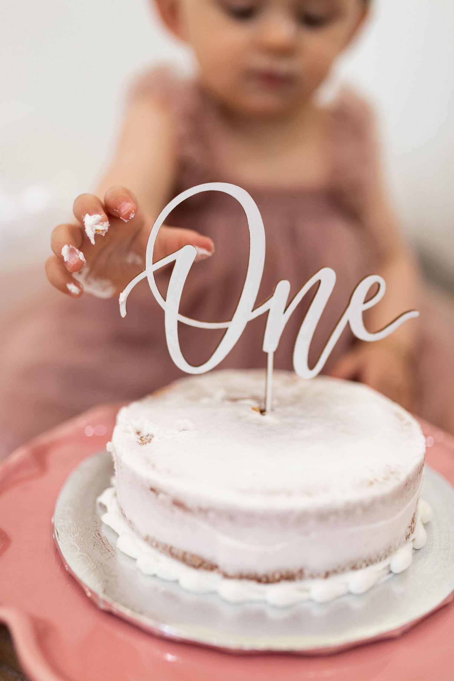 A little girl reaching towards a cake with the word one as a decoration during her cake smash at the St. Cloud studio.