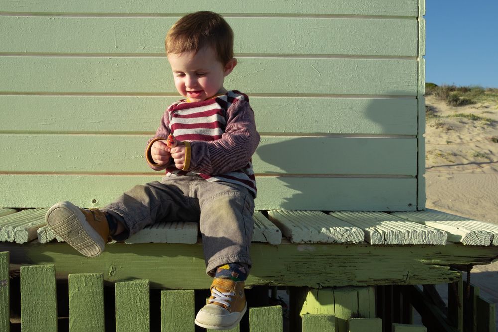 Child in striped sweater sitting on green wooden bench outdoors.