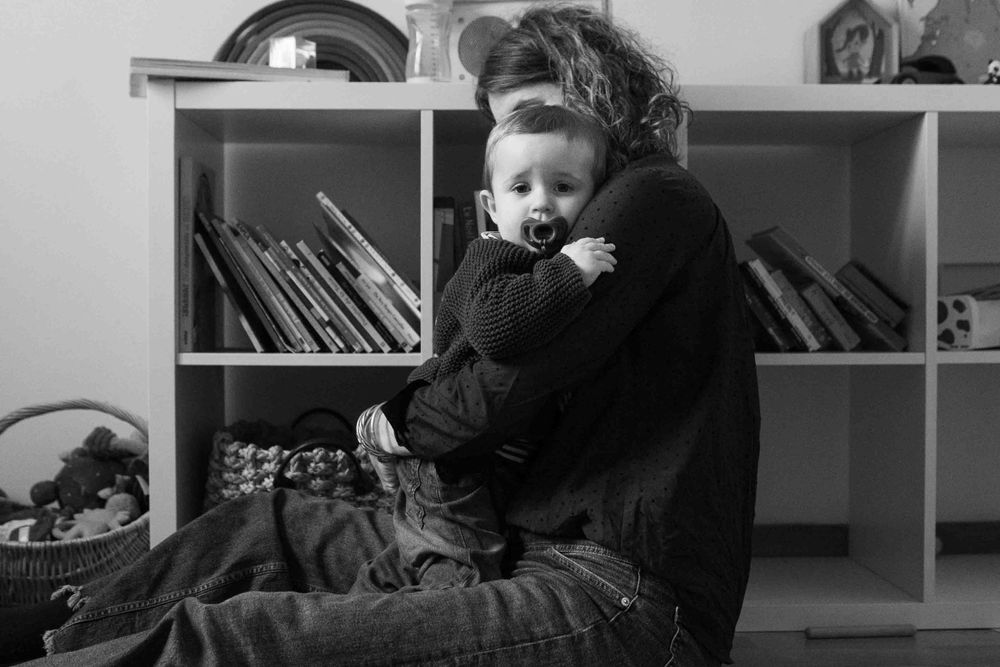 Tender black and white moment of embrace near bookshelf with children's books.