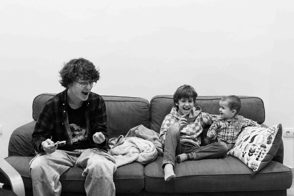 People relaxing on couch while one strums a guitar in black and white photo.
