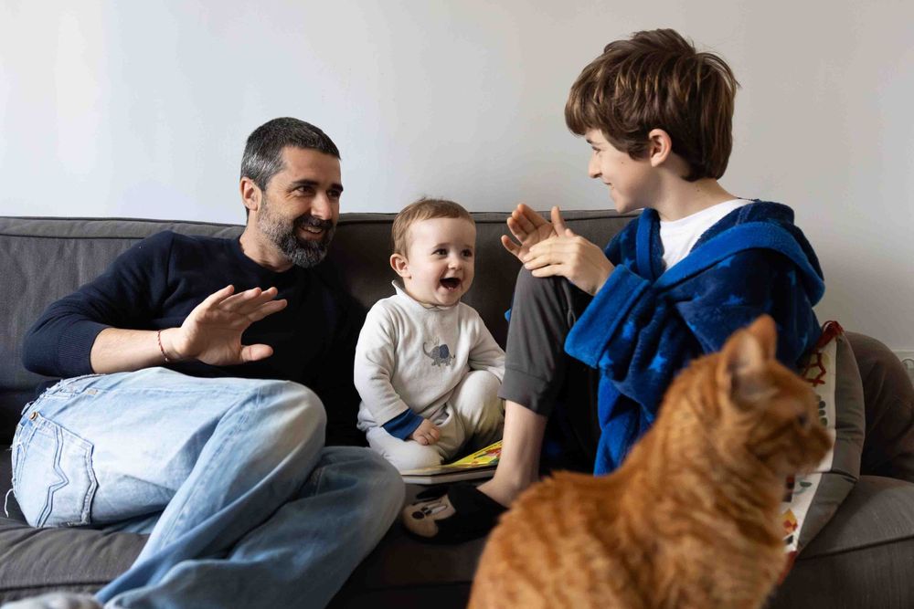 Family and cat enjoying playful moment together on gray couch.