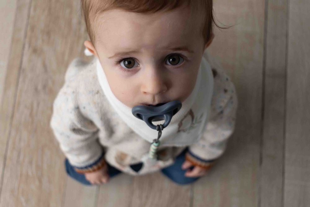 Close up view of toddler looking up at camera from hardwood floor.