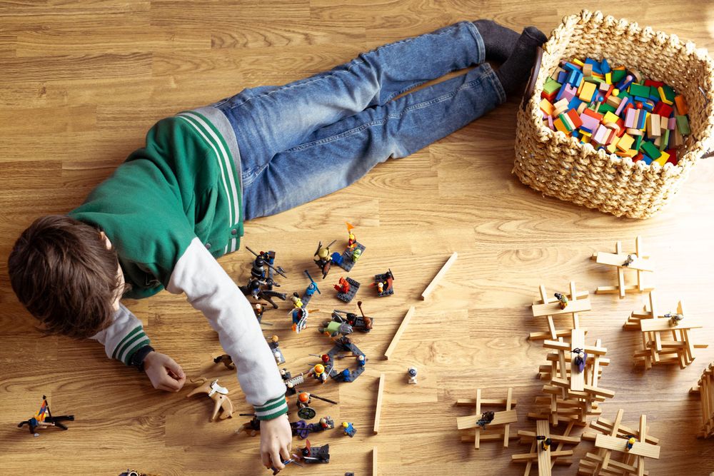 Child lying on wooden floor playing with toys and wooden blocks.