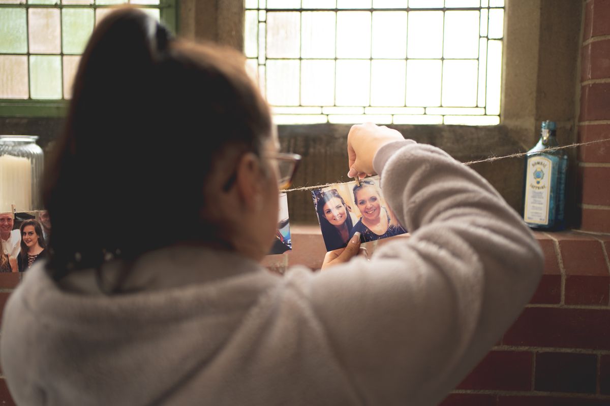 Person in gray sweater taking photos near a window in dim lighting.