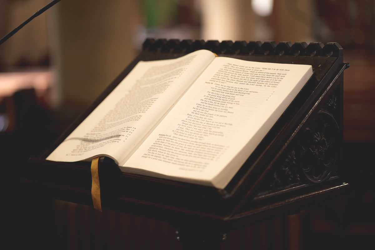 Open book displayed on black stand with golden bookmark ribbon.