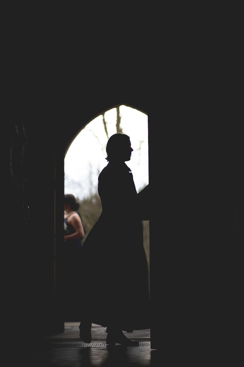 Dramatic silhouette of a figure standing in a doorway against bright background.