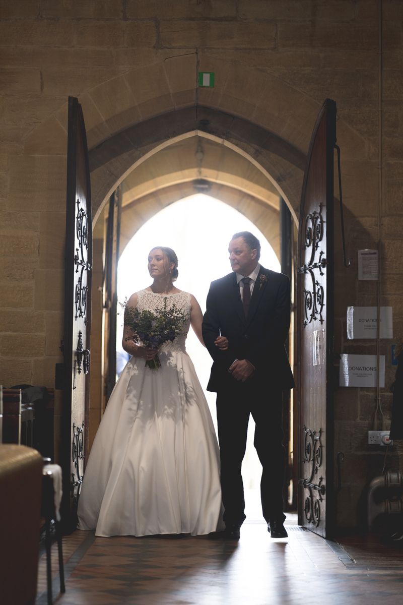 A couple entering through an ornate church doorway in formal wedding attire.