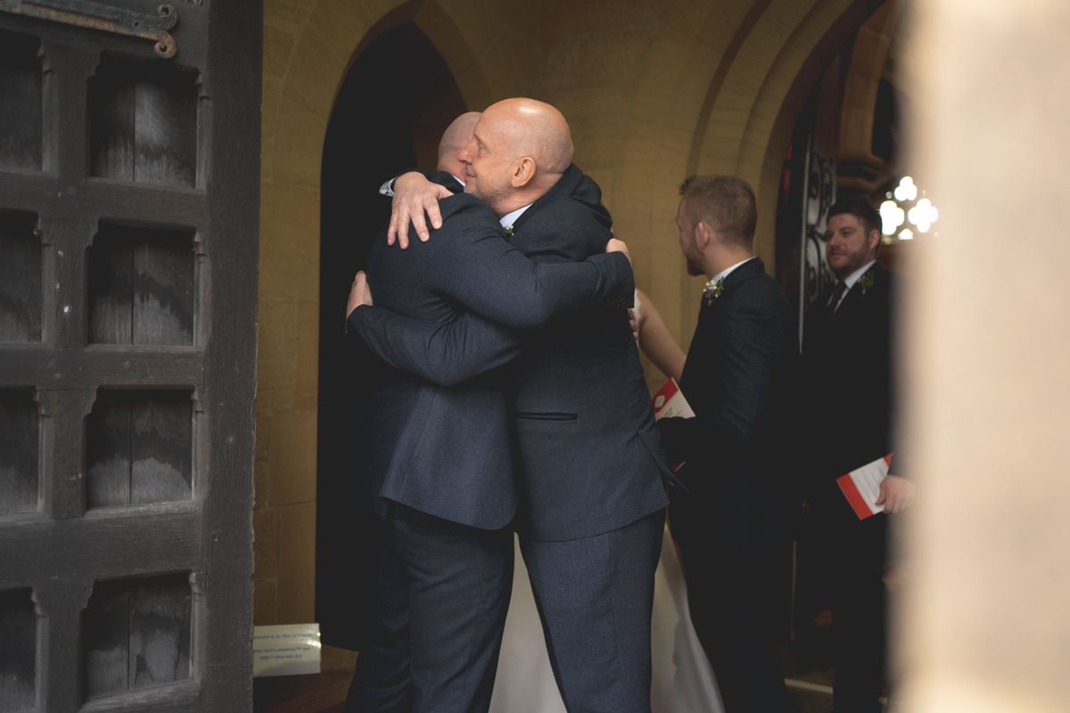 Two people share an emotional embrace under an arched doorway at a church.