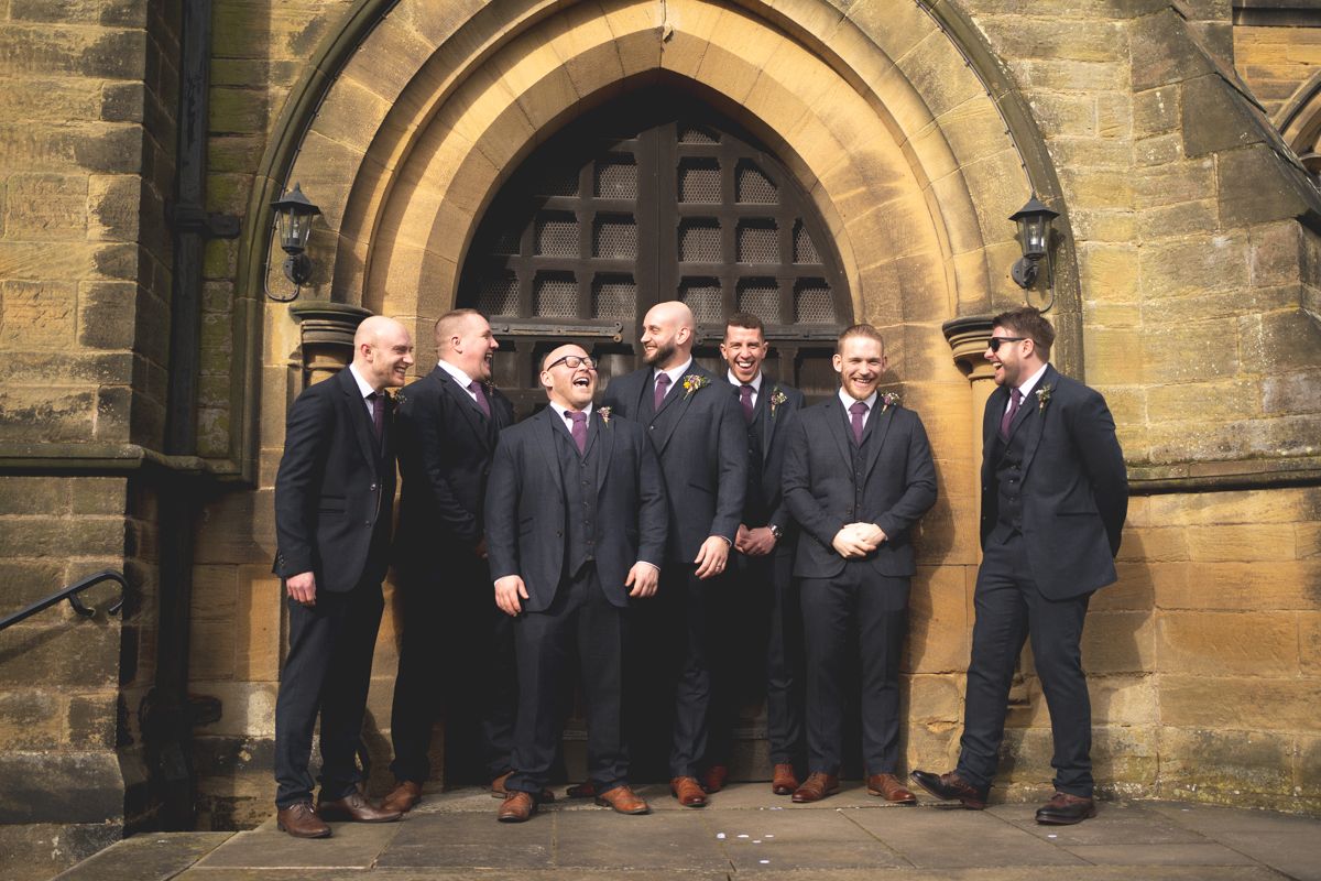 A group of formally dressed people pose together in front of a historic stone church entrance.