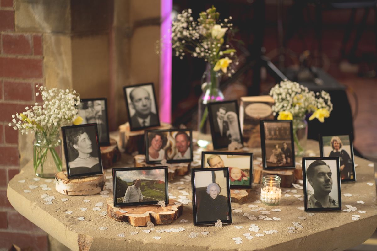 Memory table display featuring framed photographs and delicate floral arrangements at a wedding reception.