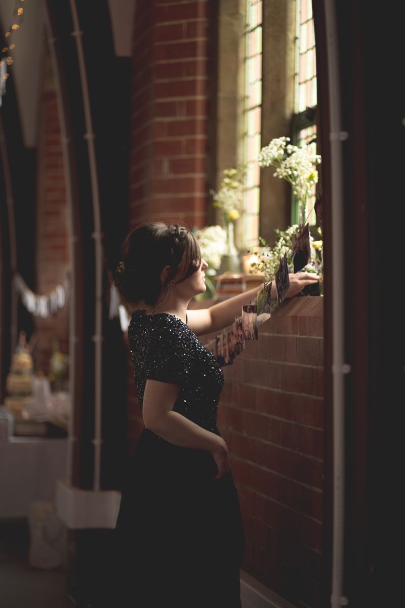 A woman in a dark dress arranges floral decorations against a brick wall at an event venue.