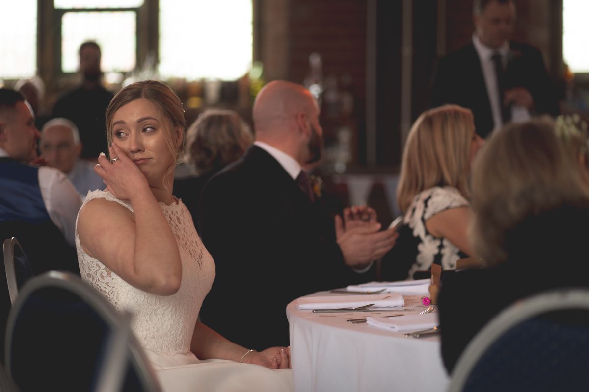 A wedding guest seated at a reception table expresses surprise during a special moment.