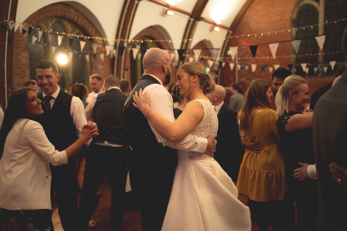 Wedding guests dance together in a historic venue decorated with bunting and string lights.