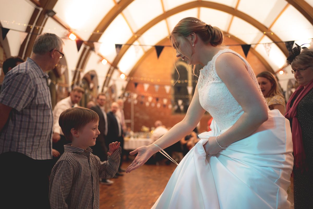 Young guest interacts with someone in a white dress during a wedding reception celebration.