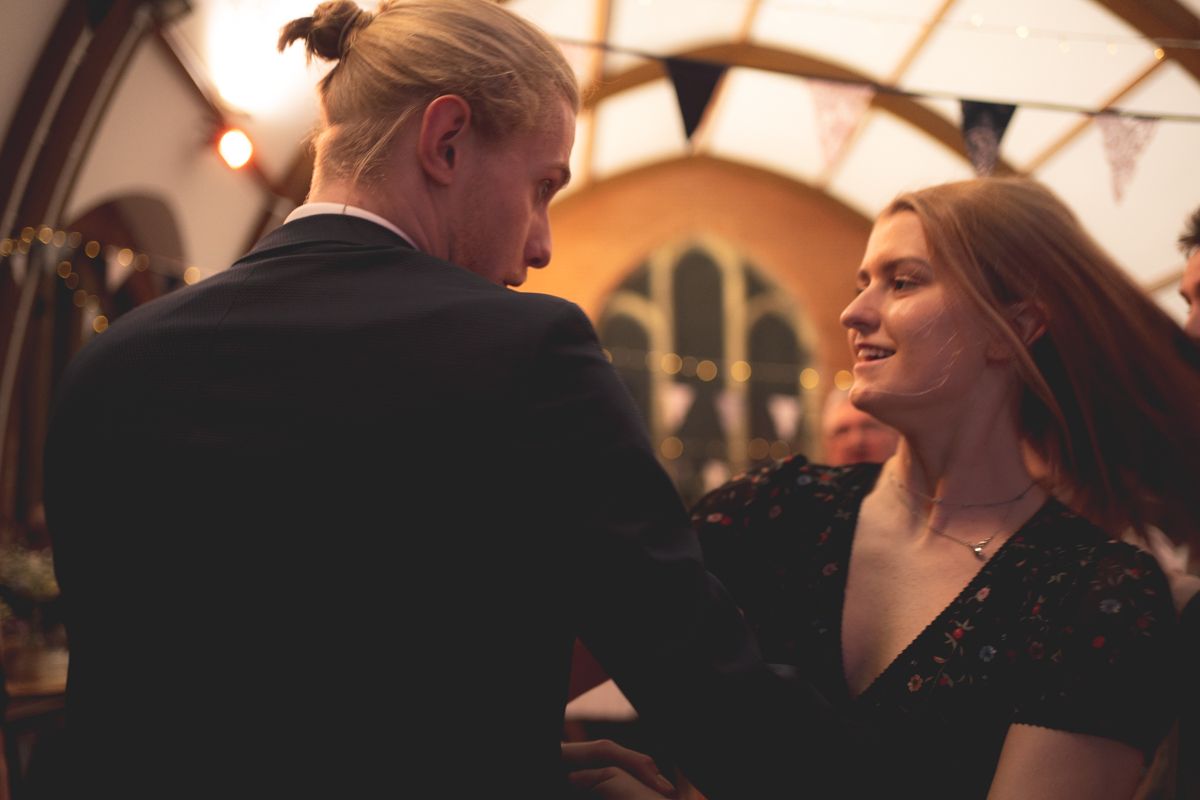 Two dancers share an intimate moment during a dance in an elegant venue with arched ceilings and warm lighting.