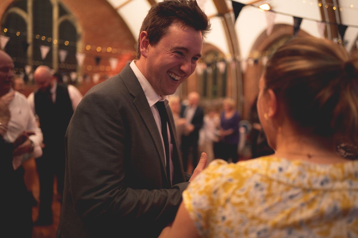 People conversing and laughing during a social gathering in an ornate hall with Gothic architecture.