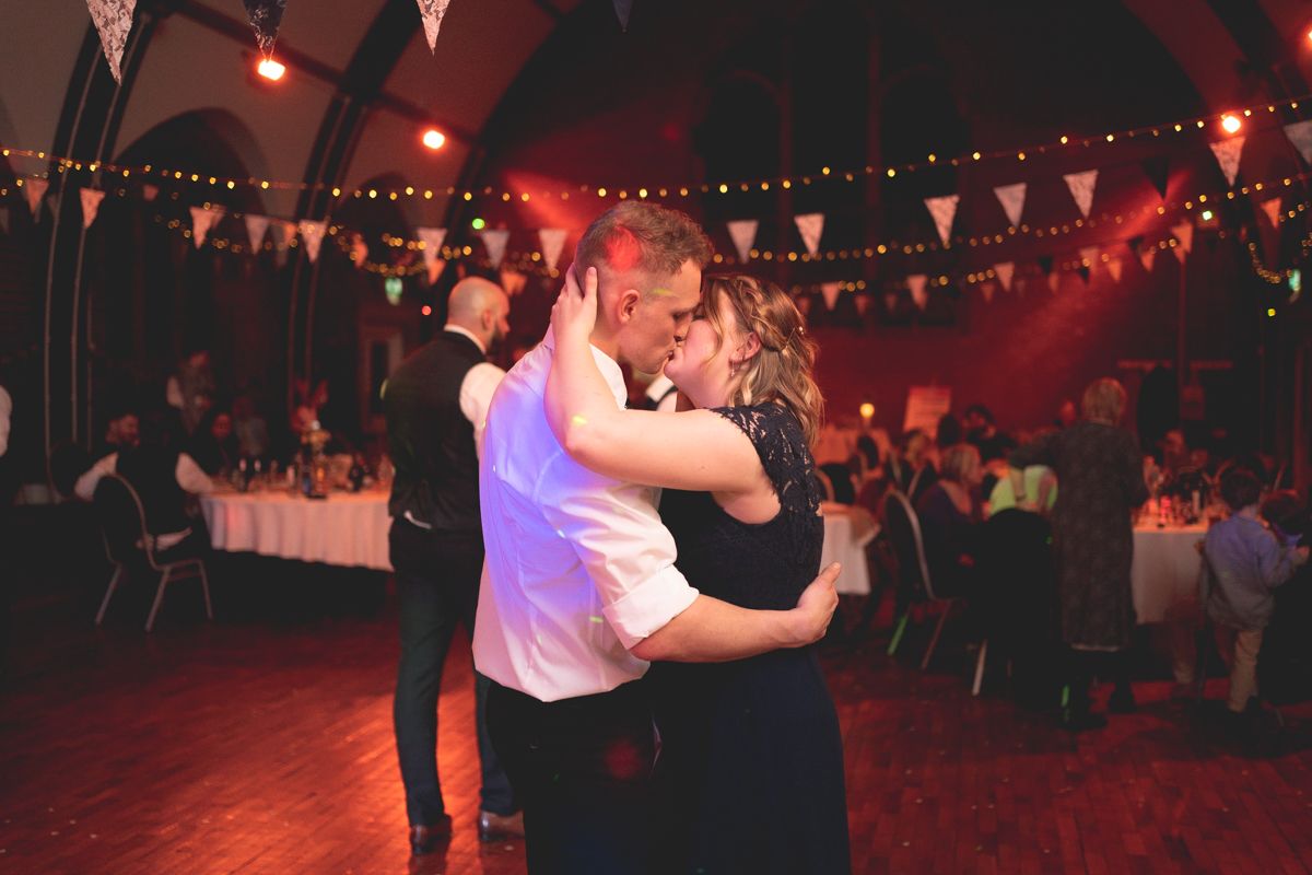 Couples dance in an atmospheric venue with red mood lighting and string lights overhead.