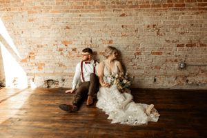 Sunlit wedding portrait with couple seated against warm brick wall backdrop.