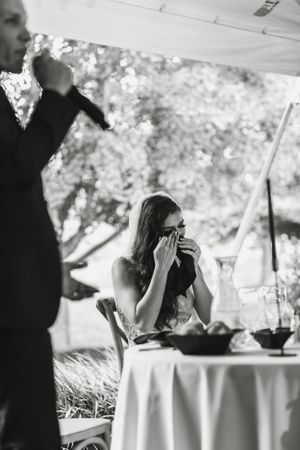 A candid reception moment captured in black and white under an outdoor tent setting.