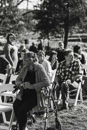 Wedding guests seated on white folding chairs at an outdoor ceremony.