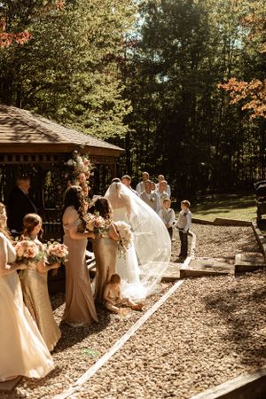 Sun-drenched autumn wedding ceremony at a rustic gazebo with flowing veil catching the light.