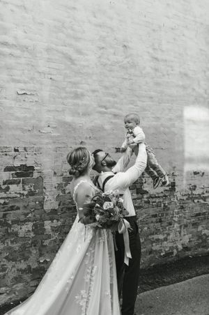 A joyful wedding moment captured in black and white against a weathered brick wall.