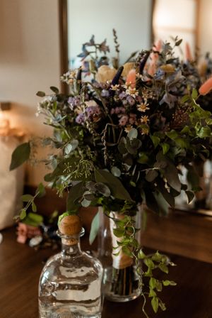 Rustic floral arrangement with dried flowers and greenery in glass bottles on wooden surface.