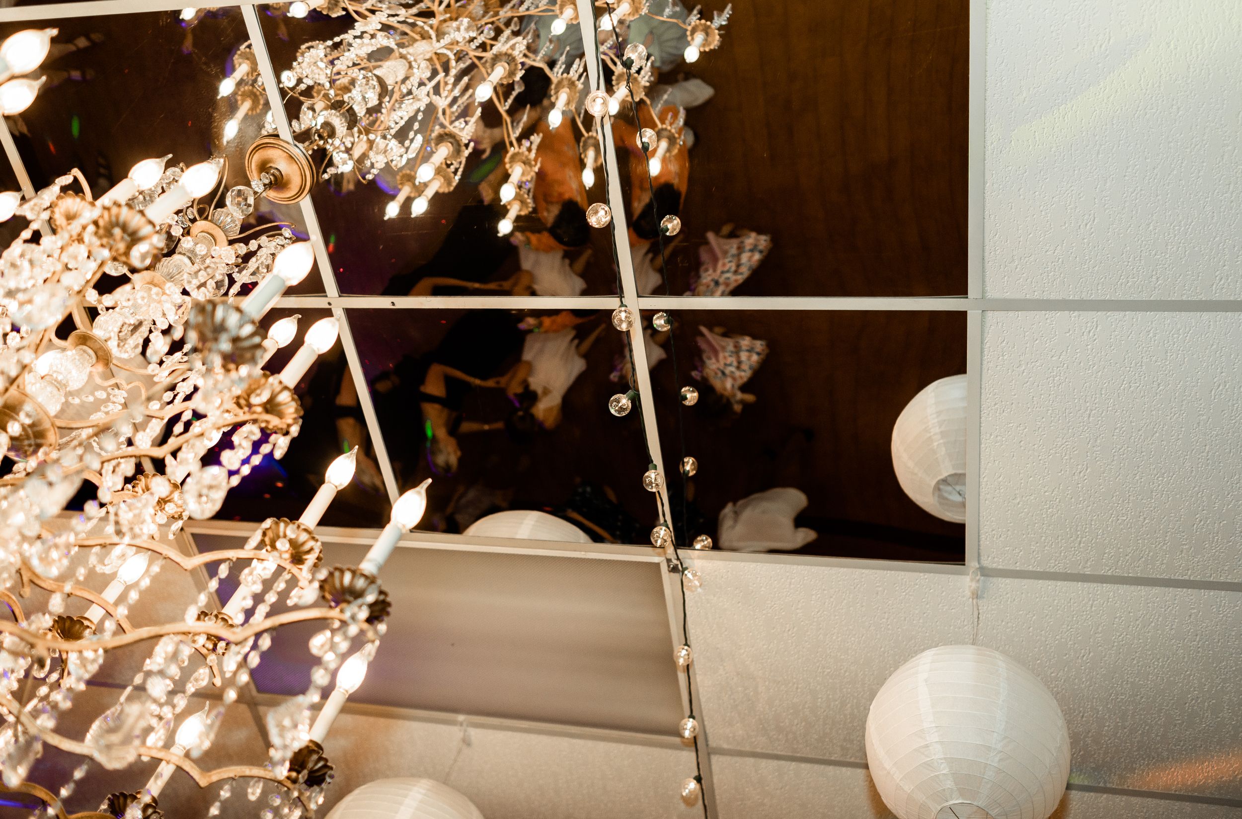 White paper lanterns and crystal chandeliers create elegant ceiling decor at an indoor venue.