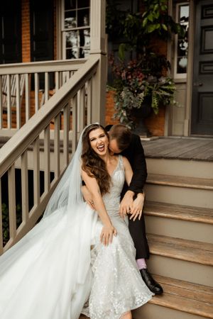 Wedding couple shares a candid moment laughing together on wooden porch steps.