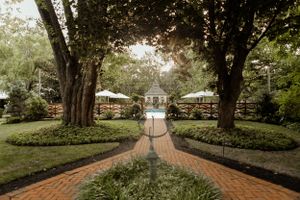 Garden wedding venue pathway with brick walkway lined by trees and white tent pavilions.