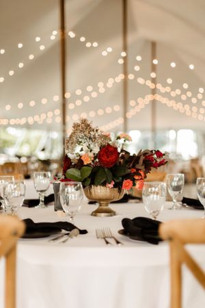 Wedding reception table setting with gold vase centerpiece under twinkling string lights.