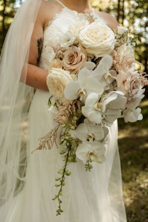 Elegant bridal bouquet featuring white orchids, blush roses, and cascading greenery.