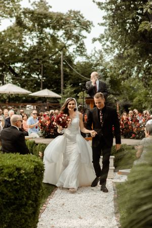 Newlyweds walk down a garden path while guests celebrate their joyful exit.