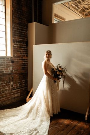 A wedding dress with a flowing train captured in dramatic lighting against exposed brick walls.