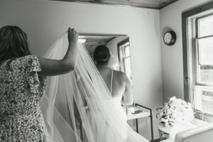 Behind the scenes preparation of adjusting a flowing white wedding veil in natural window light.