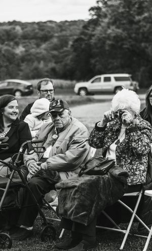 Elderly wedding guests sit in folding chairs at an outdoor gathering.